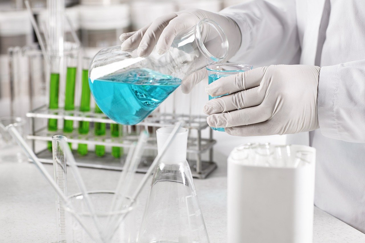 Ansicht eines Laborarbeitsplatz, blaue Flüssigkeit wird in ein kleineres Gefäß gegossen