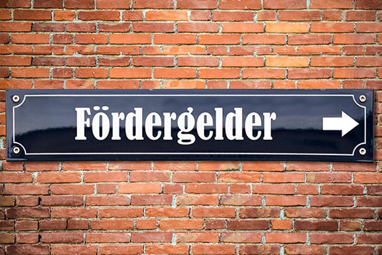 auf einer Ziegelmauer ist ein dunkelblaues Emaille-Schild mit der Aufschrift Fördergelder und einem Pfeil nach rechts in weiß